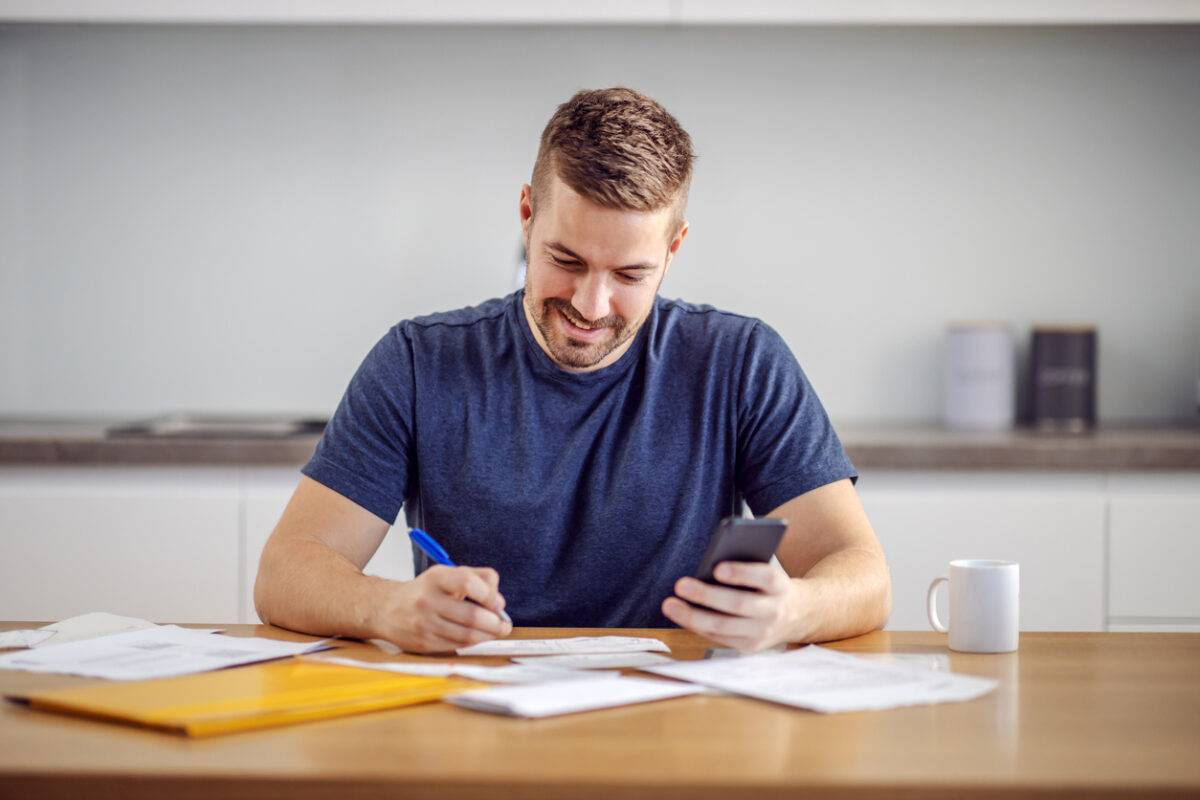 Young handsome smiling bearded man sitting at home, calculating budget for a buy-to-let