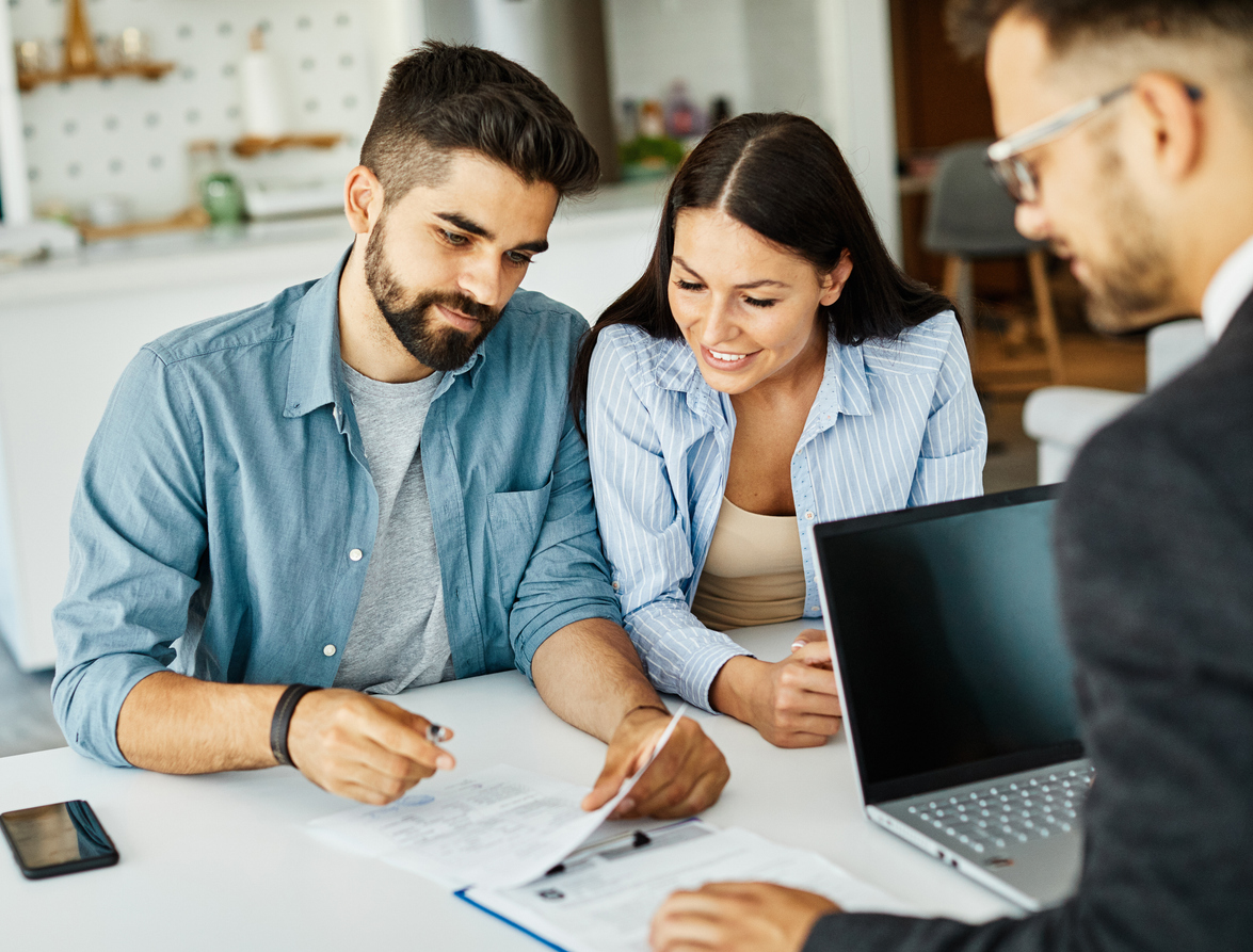 Young happy couple sat at desk with a professional man with paperwork and laptop