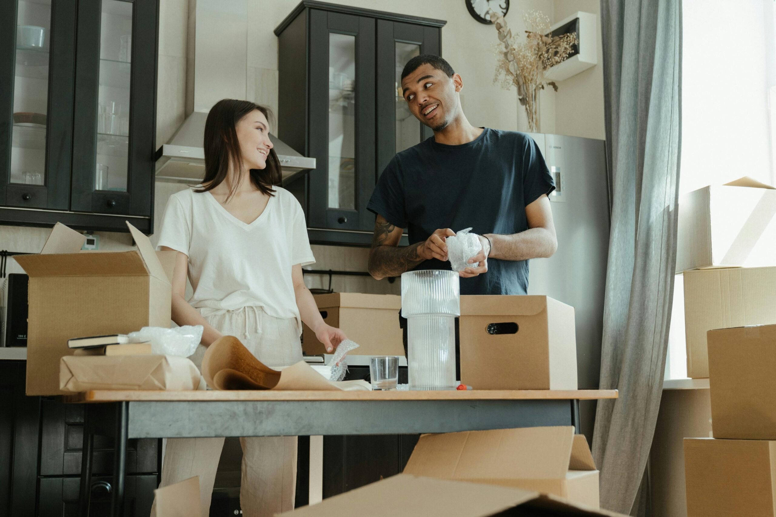 young male a female couple looking happy packing moving boxes in their kitchen getting ready to move house