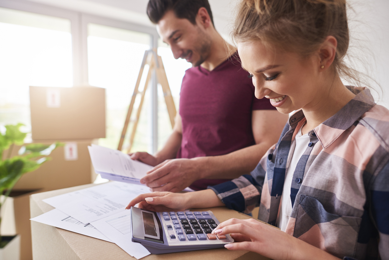 twentysomething year old Male and female couple with calculator, paperwork and moving boxes looking happy.