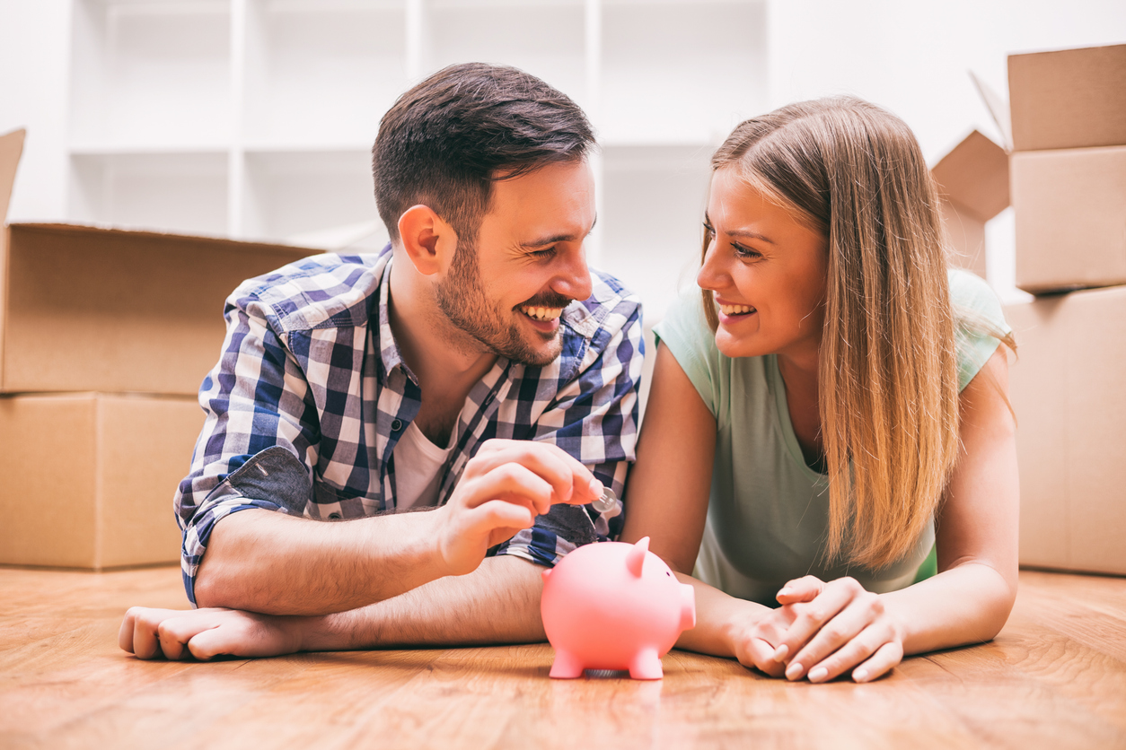 young male and female couple looking at each other happily as they put money in a piggy bank