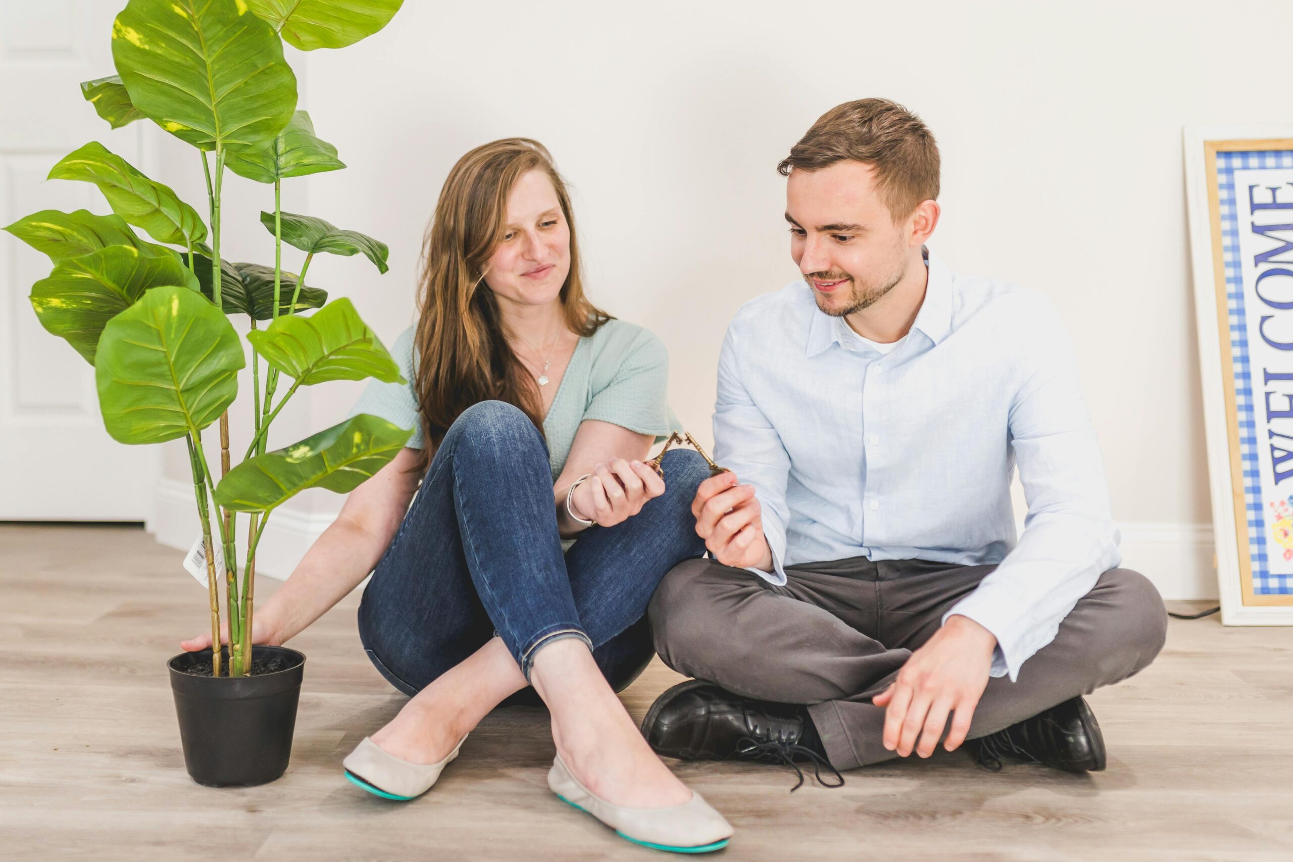 Young male and female happy couple sat on the floor clinging keys together with moving boxes and a houseplant